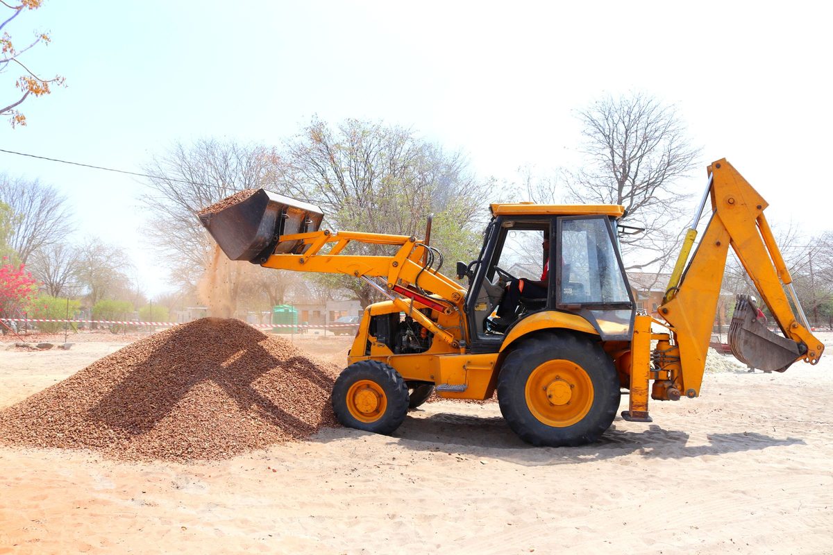 Backhoe loader dumping a bucket of gravel onto a pile at a work site