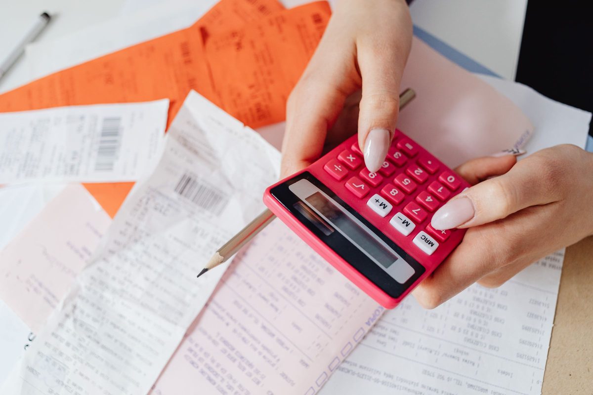Hands working a pink calculator over a pile of receipts