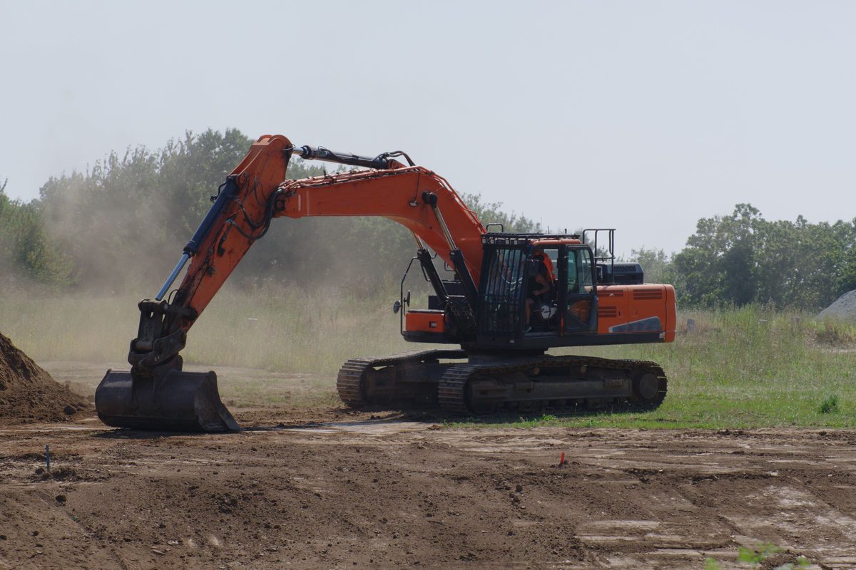 Orange excavator digging into bare ground at a cleared site