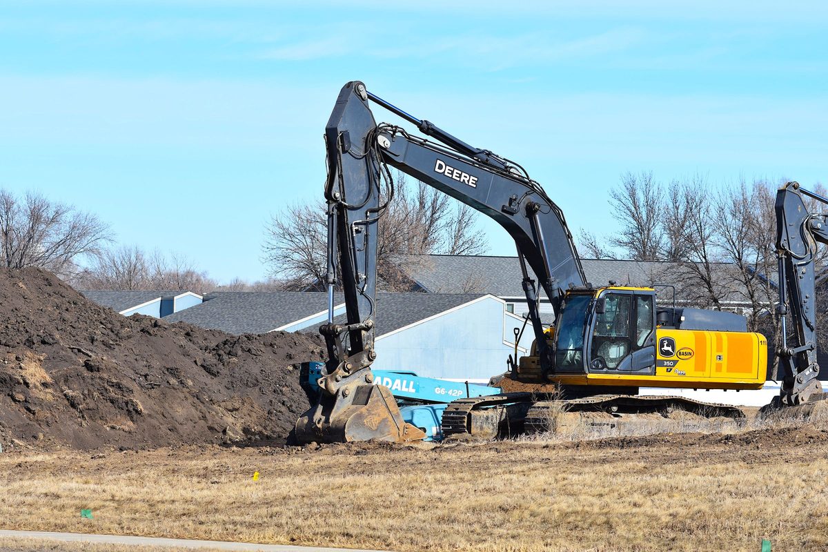 Excavator beside a pile of dirt near a row of houses